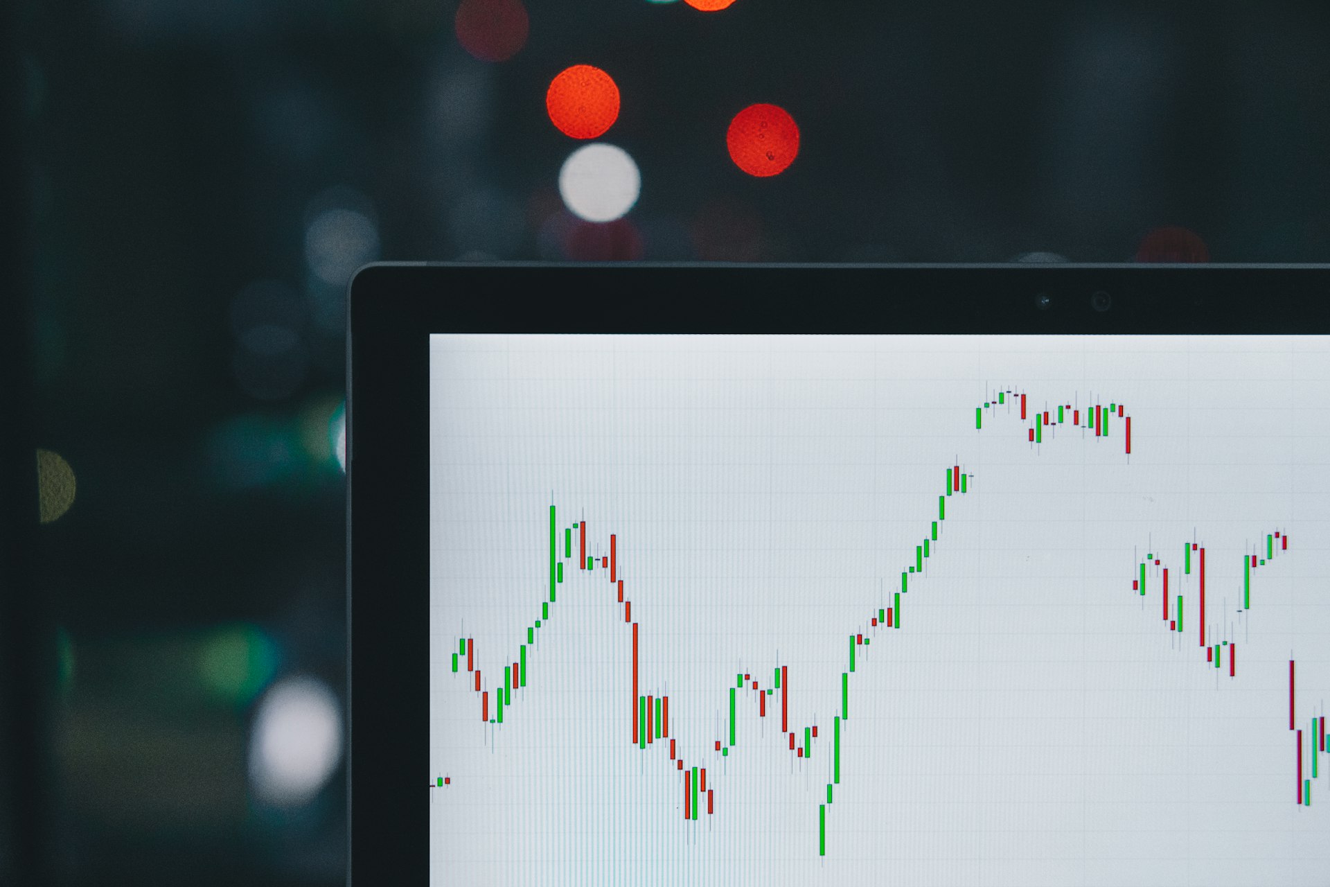 Laptop screen showing a green and red candlestick chart in a dark room